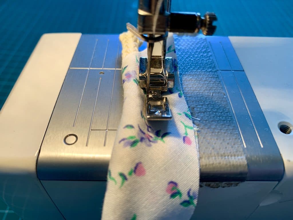 a zipper foot sewing the cording into place within the bias binding to create piping.